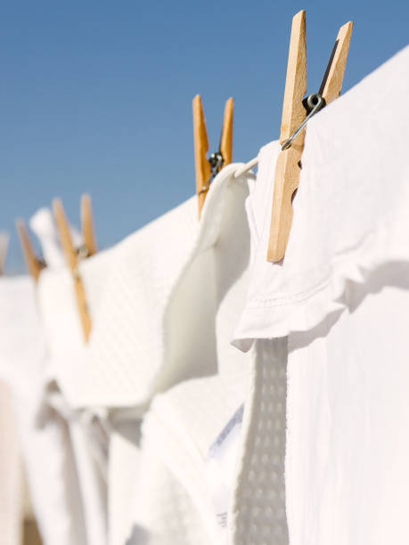 White clothes hung out to dry on a washing line in the bright warm sun. Background is a clear blue sky. stock photo