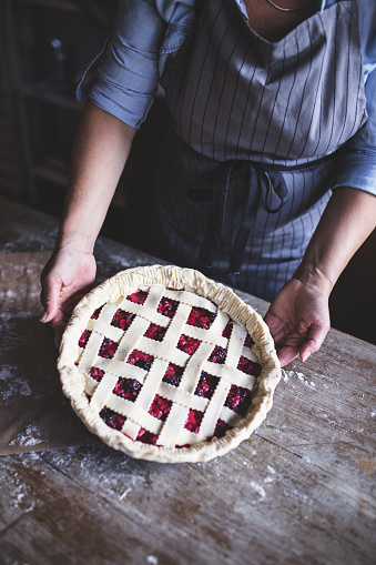 Delicious Homemade Cherry Pie Ready For Baking, woman holding pie in her hands, wooden table