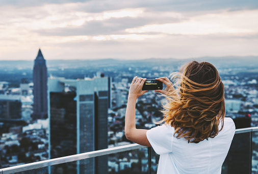 Young woman takes photo with mobile phone above Frankfurt, Germany