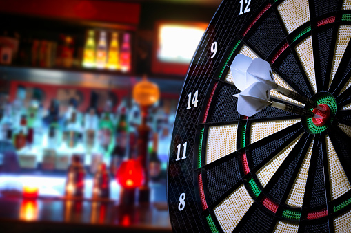 Cutout of three darts, two red and one green hitting bull's eye spot on on a tilted dart board isolated over white background denoting success, win, achievement of business target, competition