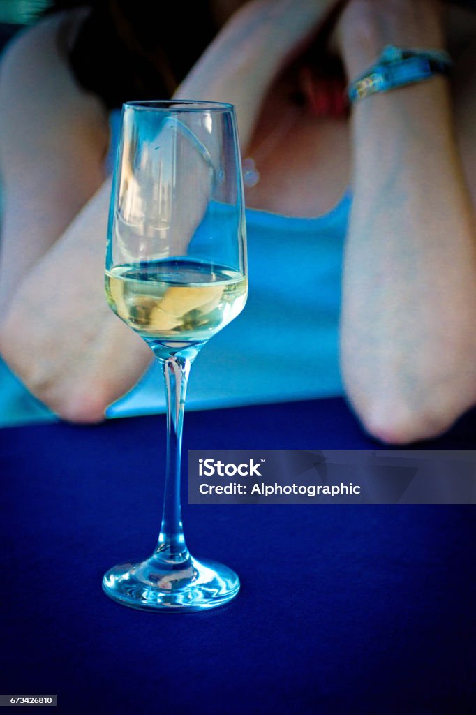 White wine glass on a street cafe table White wine glass on a tablecloth with an unrecognisable woman in the background. Chablis Wine Stock Photo