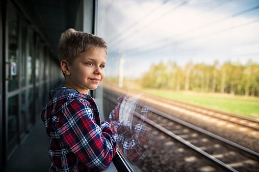 Little boy aged 7 standing in train corridor and looking out of the window.\n