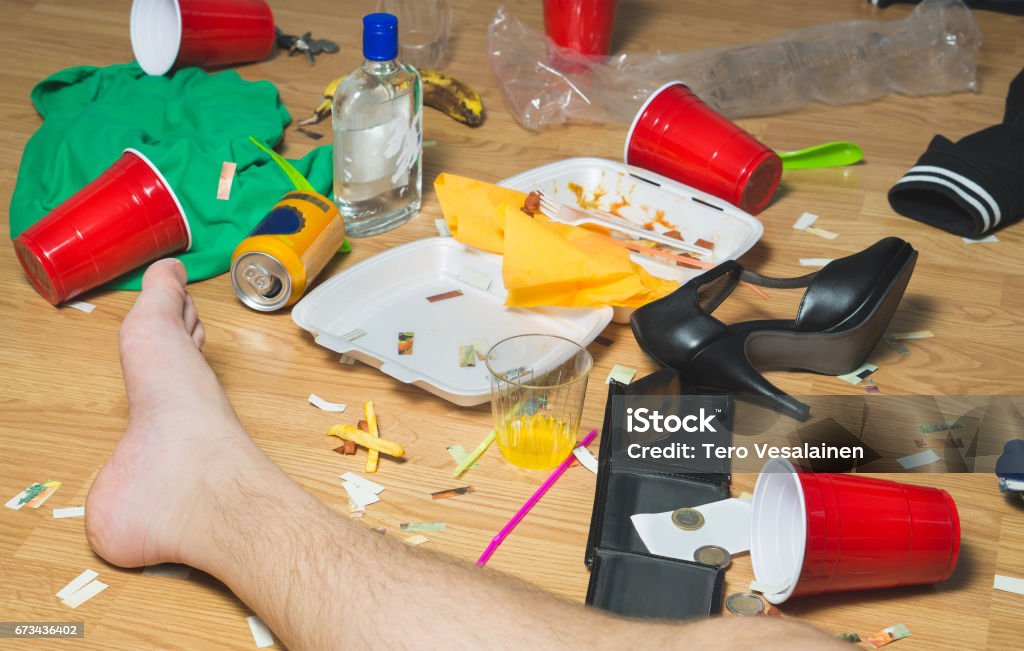 Planait sur l’homme évanoui sur le sol le jour suivant à une fête, des pieds visibles. Trash, restes de nourriture, des vêtements, des talons hauts et bouteilles partout dans la maison malpropre. - Photo de Confetti libre de droits