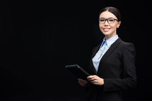 brunette businesswoman in black suit using digital tablet isolated on black
