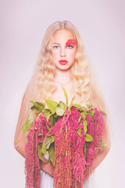 Close up portrait of young nordic blonde woman in hooded jacket while smelling a beautiful flower of the sea dunes - Fabulous magnetic gaze and fairytale style - Skin Care concept