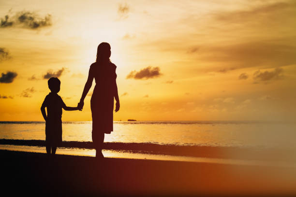 istock mother and son walking on sunset beach 673465444