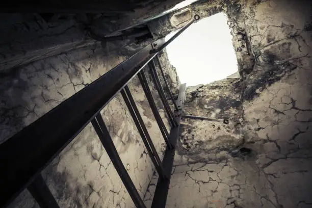 Old empty abandoned bunker interior with rusted metal ladder going up to glowing manhole