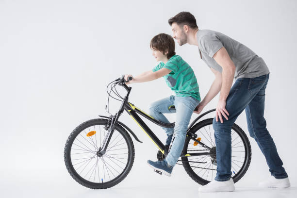 Happy mixed-race boy and his father cycling in the park