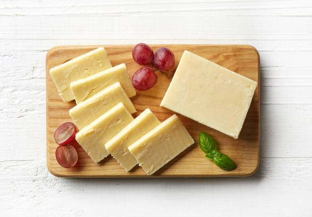 Piece and slices of white cheddar cheese Cutting board of white cheddar cheese on white wooden background. From top view cheddar cheese stock pictures, royalty-free photos & images