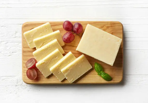 Cutting board of white cheddar cheese on white wooden background. From top view