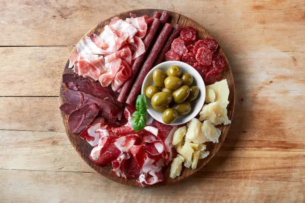Cold smoked meat plate with prosciutto, salami, bacon, cheese and olives on wooden background. From top view