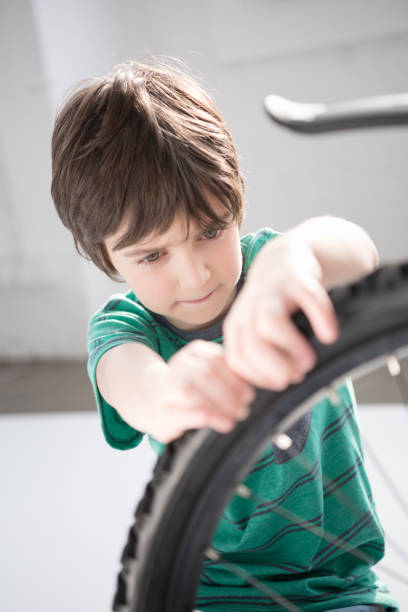 istock Concentrated little boy checking bicycle tyre indoors 673499432