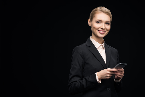 smiling businesswoman using smartphone isolated on black
