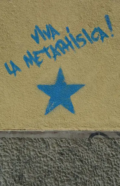 Long live the metaphysics! The text is written in Spanish language above the blue star painted on the dirty ochre and gray wall. A concept photograph. A post processed photograph.