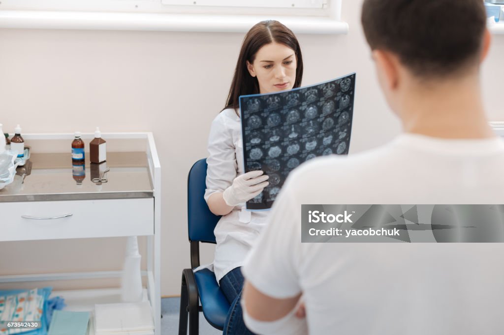 Serious professional doctor examining the X ray photo Medical diagnostics. Serious professional female doctor sitting on the chair and examining the X ray photo while working Shock Stock Photo