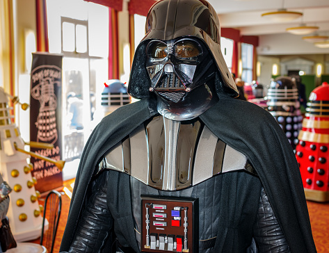 'Darth Vader' from 'Star Wars' walks through hall at Sci-Fi Scarborough with 'daleks' from 'Doctor Who' in the background.