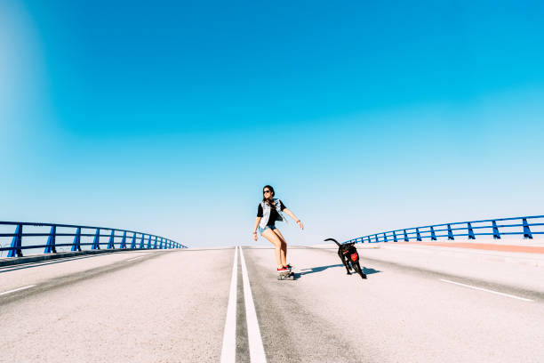 Beautiful young skater playing with her dog in the city.
