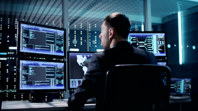 Back View of Technical Controller/ Operator Working at His Workstation with Multiple Displays. Possible Power Plant/ Airport Dispetcher/ Dam Worker/ Government Surveillance/ Space Program