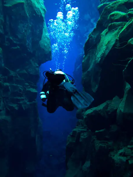 Photo of Single Diver Action Shot Swimming Through Continental Split at Silfra in Deep Section at Pingvellir National Park with Bubbles