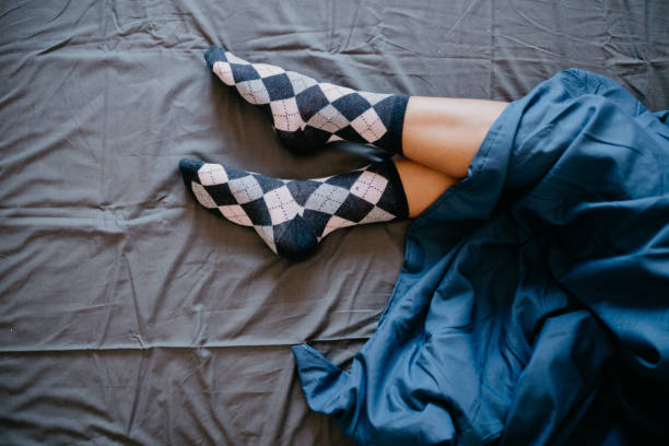 gambe da donna coperte di lenzuolo blu - bed human leg home interior comfortable foto e immagini stock