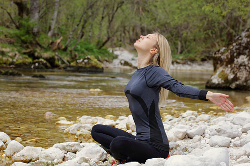 Happy smiling young woman breathing fresh air, relaxing in nature, doing stretching exercises. Freedom concept