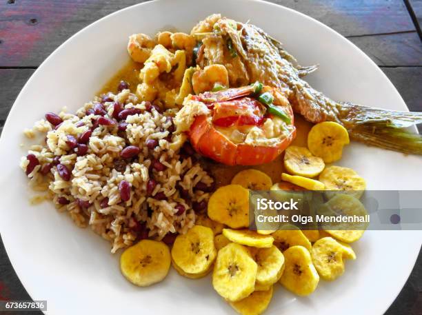 Local Food Lobster Red Snapper Fish Shrimp Rice Beans Fried Plantains Coconut Milk Sauce Roatan Honduras Creole Unique Traditional Cuisine Delicious Seafood Lunch Meal Rustic Wood Background Stock Photo - Download Image Now