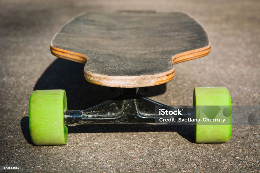 Vecchio longboard usato a terra. Skateboard nero su una strada asfaltata vuota. Profondità di campo superficiale. Da vicino. - Foto stock royalty-free di Scontornabile