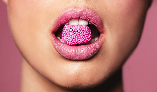 Beautiful pink lips with a piece of sweet candy. Close up of young woman with candy in mouth.