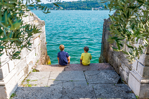 boys sitting on a dock looking at the beautiful lake garda in italy