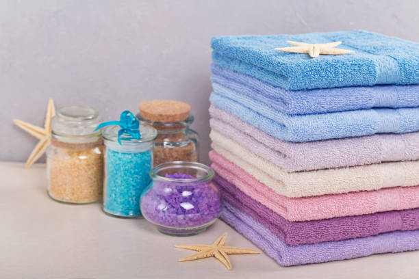 hoher stapel von bunten badetüchern mit meersalz auf leichtem hintergrund. pastell farben baumwolltücher. hygiene-, stoff-, spa- und textilkonzept - softness textile pink terry cloth stock-fotos und bilder