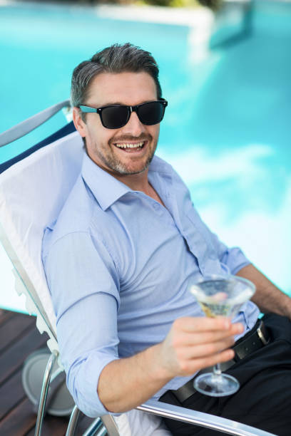 istock Smart man holding martini glass while relaxing in sun lounger 673688154