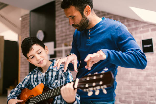 Guitar Lessons Guitar Lessons. Boy Learning to Play Guitar on guitar lessons with his father or male teacher. He is  teaching him playing the instrument father and son guitar stock pictures, royalty-free photos & images