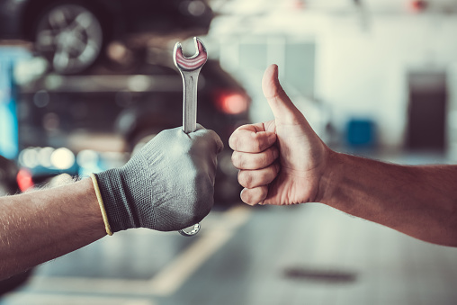 Cropped image of mechanics working in auto service. One is holding a spanner while the other is showing Ok sign