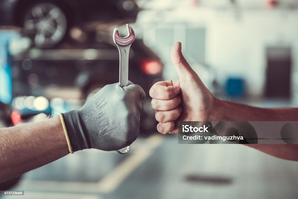 Handsome auto service workers Cropped image of mechanics working in auto service. One is holding a spanner while the other is showing Ok sign Auto Repair Shop Stock Photo