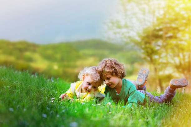 Two brothers spending time together in green park outdoors with older boy watching baby brother with love and affection