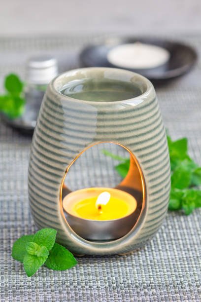 istock Peppermint essential oil in aroma lamp on gray mat with spa background, vertical 673766034
