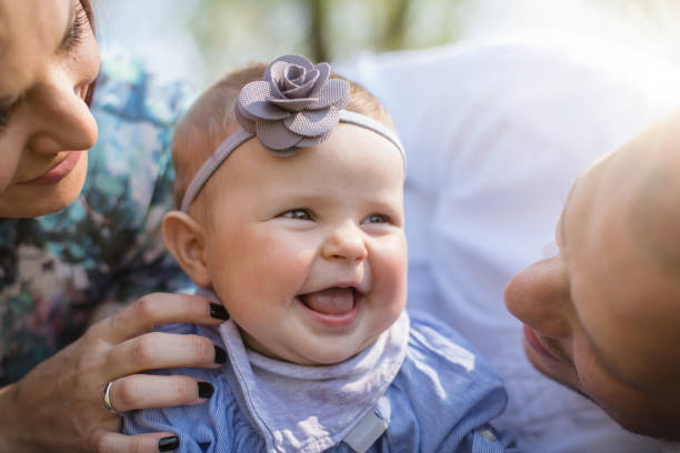 Little baby girl is surrounded by her parents love on a beautiful day outside.