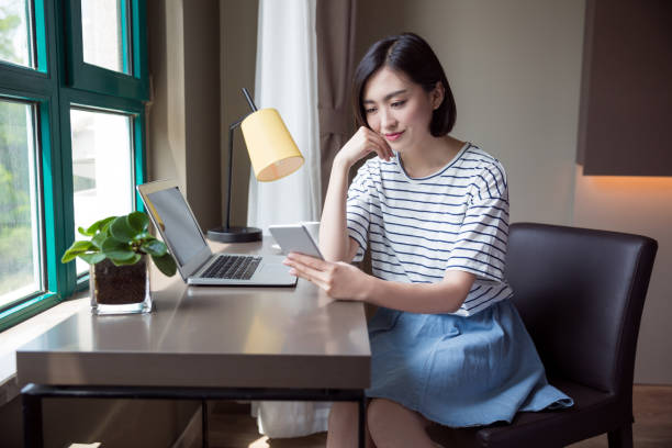 beautiful woman using smartphone with a laptop on desk at home stock photo