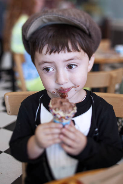 ładny mały chłopiec w brązowym newsboy gatsby drivng cap i smoking t-shirt jedzenia niechlujny stożek lodów czekoladowych - drivng zdjęcia i obrazy z banku zdjęć
