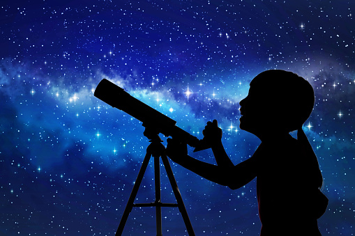 Silhouette of little girl looking through a telescope at the stars background