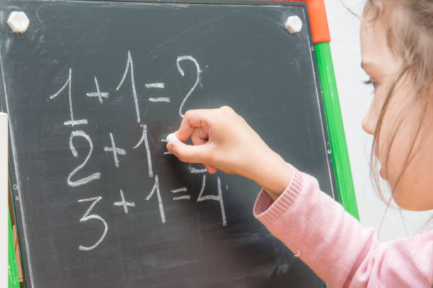 istock girl at a board solves examples on mathematics. Training of the child. 673791720