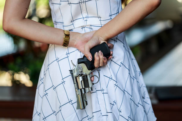 istock Young pretty Asian woman hiding a hand gun behind her back with both hands. 673797920