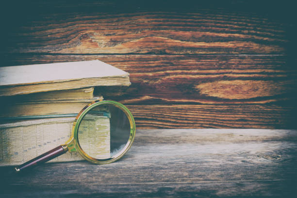 istock A stack of old books and a magnifier on a wooden background with space for text. Retro toning with vignette 673843632