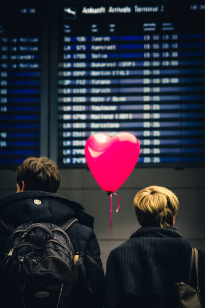 Munich, 3rd February 2017: A couple wait for somebody in the Arrivals section of Munich Airport (MUC) with a pink heart shaped balloon. stock photo
