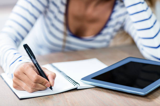 istock Midsection of woman writing in notebook by digital tablet 673847170