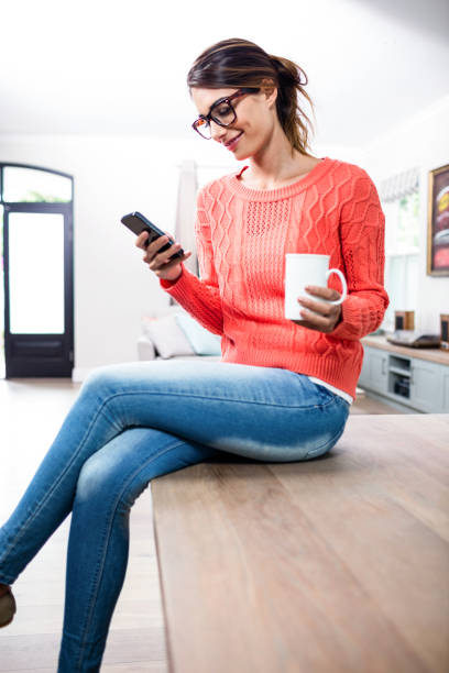 istock Young woman with mobile phone and mug sitting on table 673847836