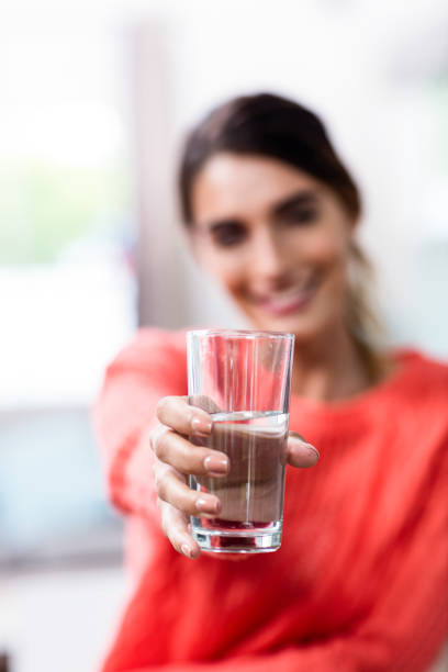 Young woman showing drinking glass with water Happy young woman showing drinking glass with water at home wavebreakmedia stock pictures, royalty-free photos & images