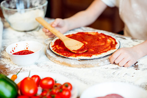 partial view of girl putting tomato sauce on pizza dough