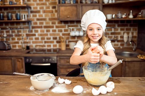 little girl in chef hat making dough for cookies