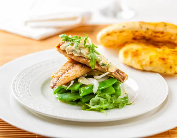 Smoked mackerel on a bed of green beans topped with sauce and rocket leaves.